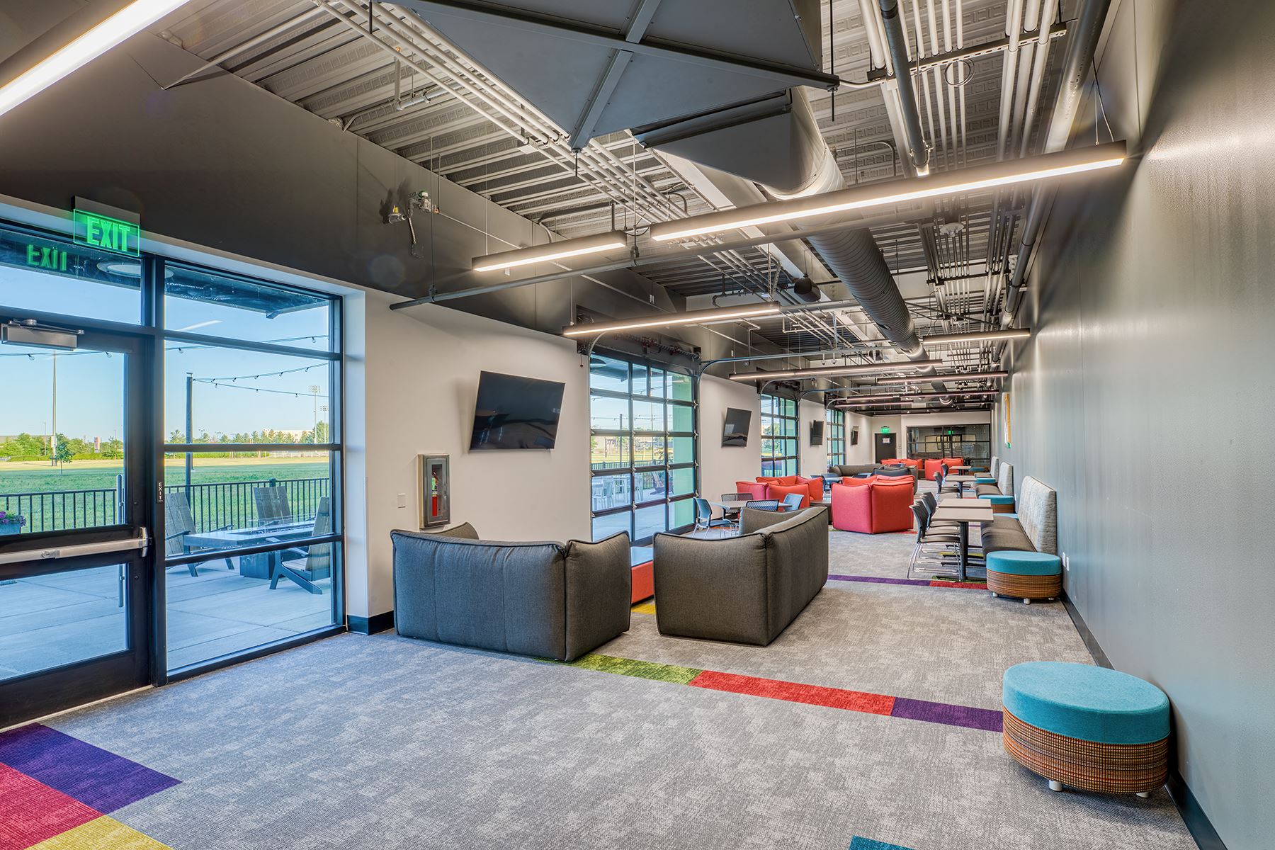 An image of a long, narrow room with cushioned seating, tables and large windows